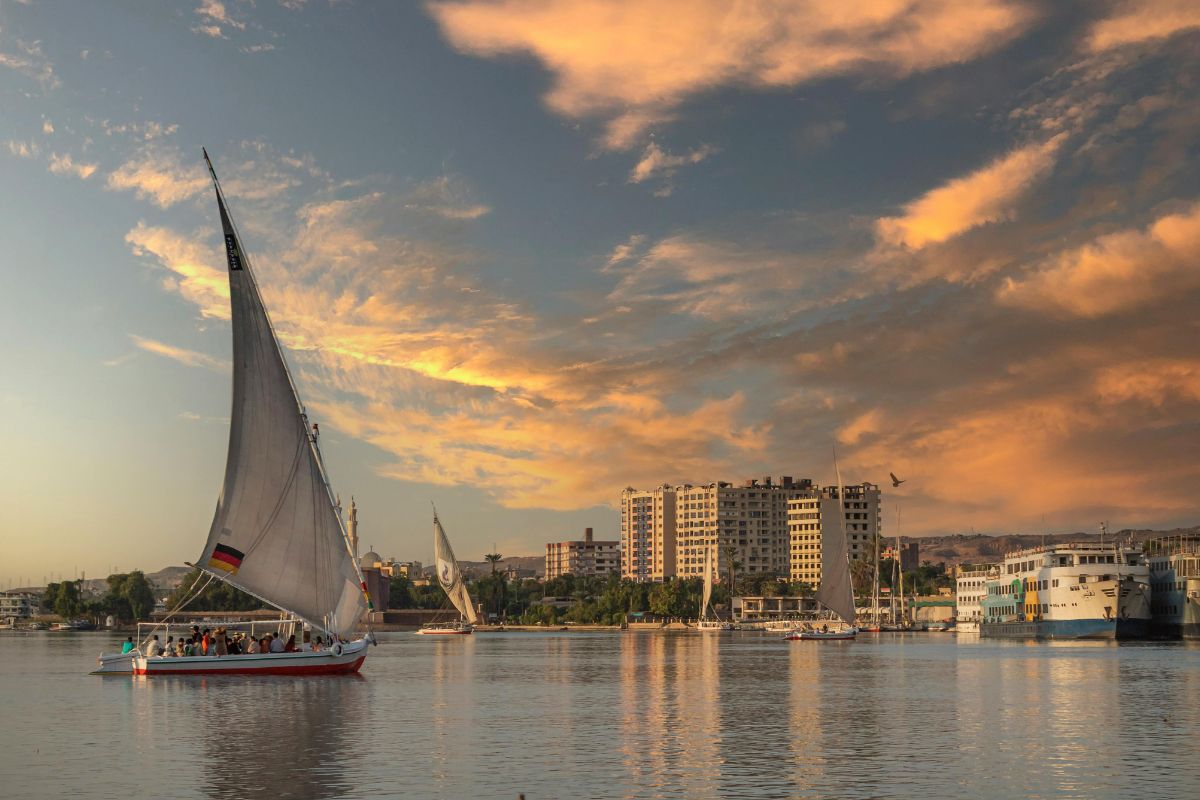 Traditional Egyptian felucca sailboat gliding on the Nile River at sunset with a city skyline in the background